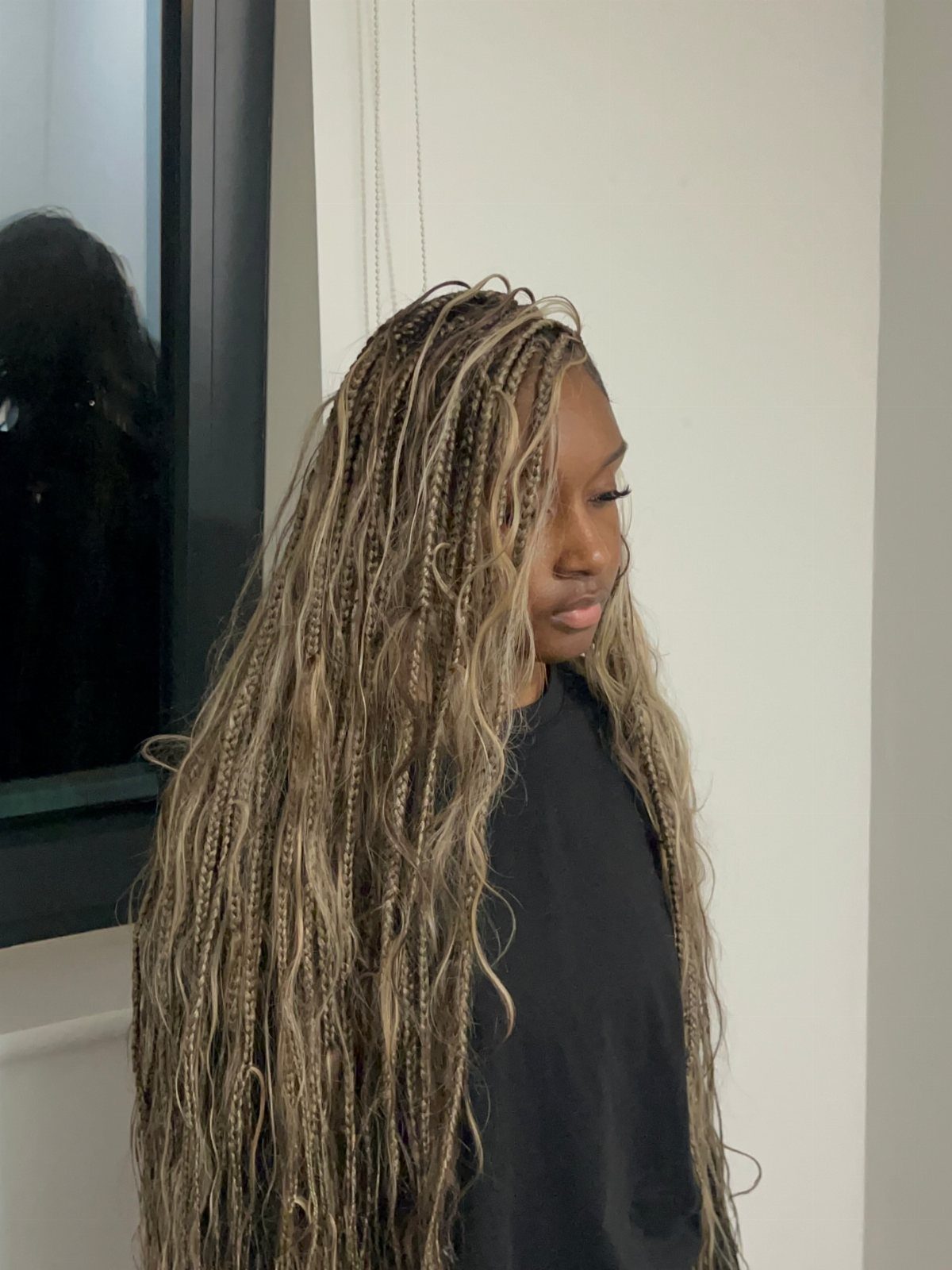 Side-profile person wearing long sun-kissed blonde braids with dark roots indoors