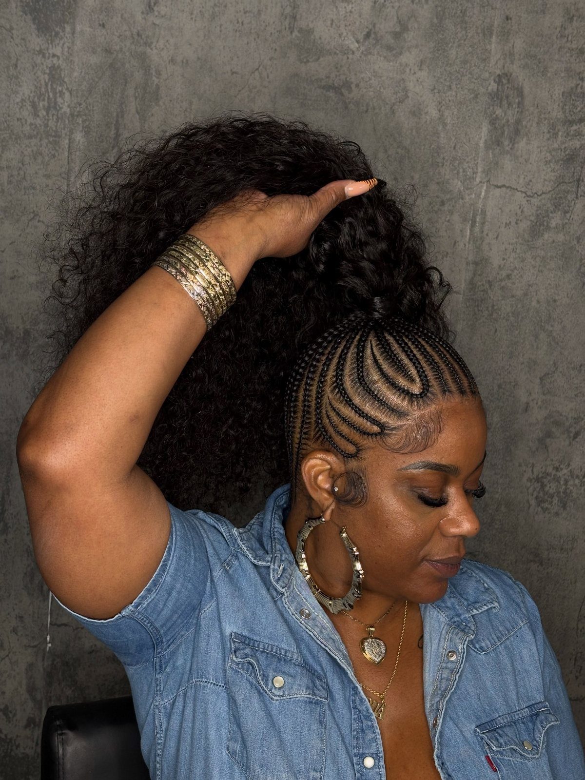 Woman lifting a curly braided high puff above neat cornrows