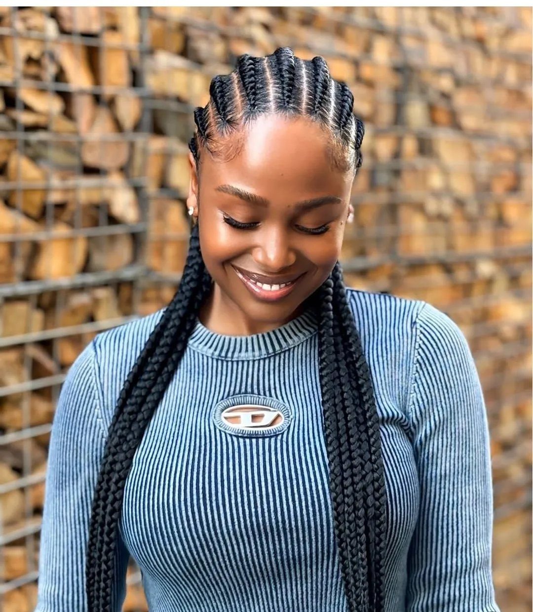 Large black cornrows continue into long braids over a blue-gray top