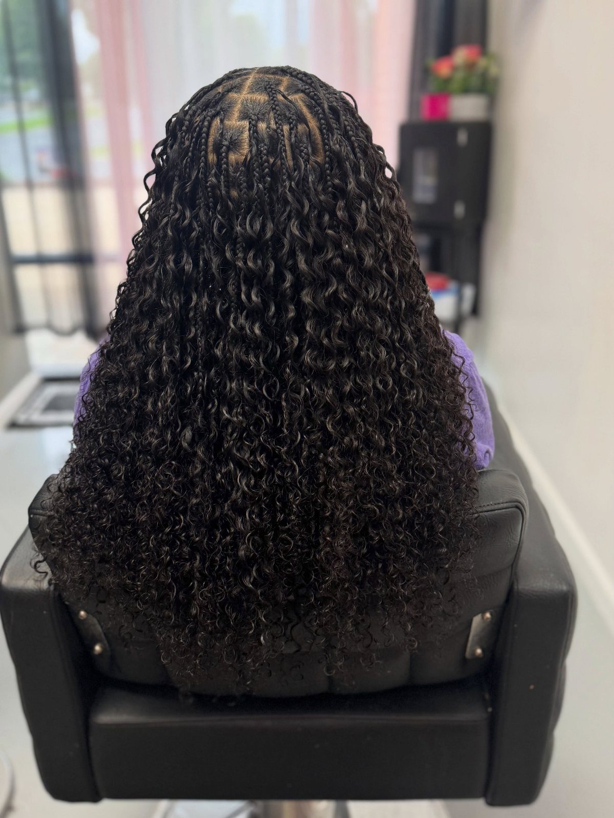 Braided crown flowing into long, voluminous black curls in a salon chair