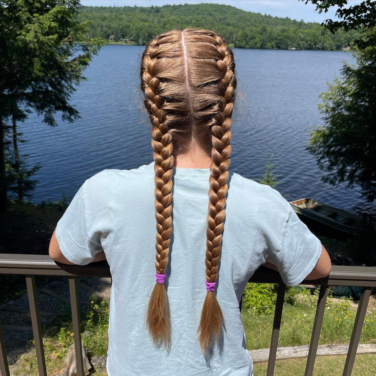 Two long brown pigtail braids hang down a person's back by a lake