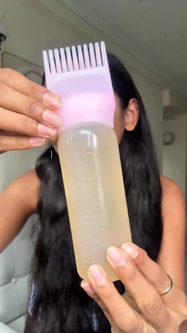 Comb applicator bottle held in front of a person’s long dark hair