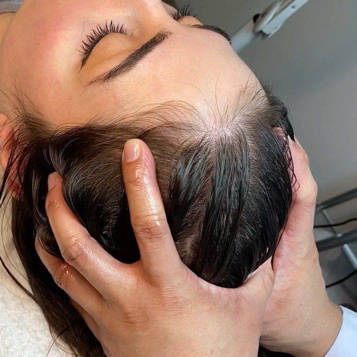 Hands massage a person's wet dark hair and scalp