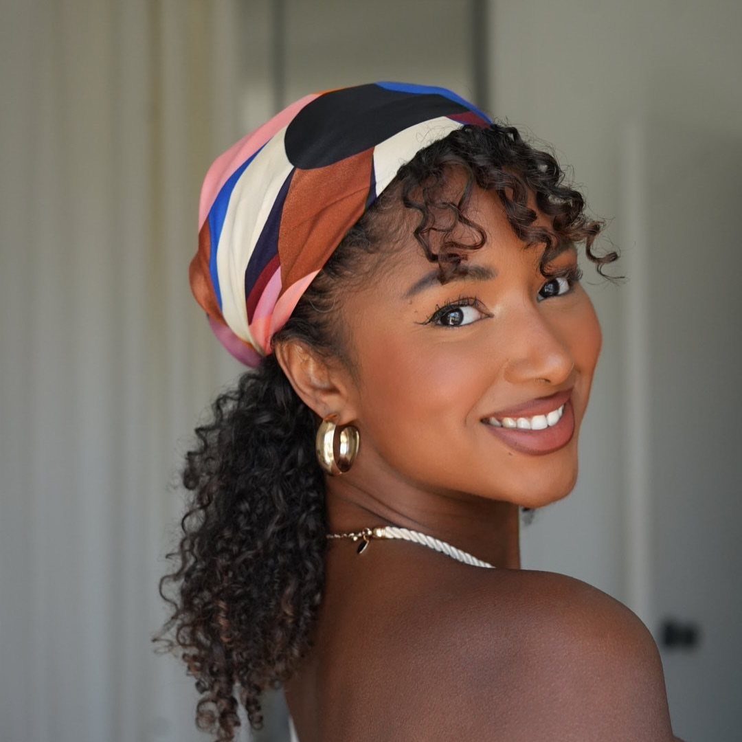 Woman wearing a colourful headwrap with loose curls framing her face