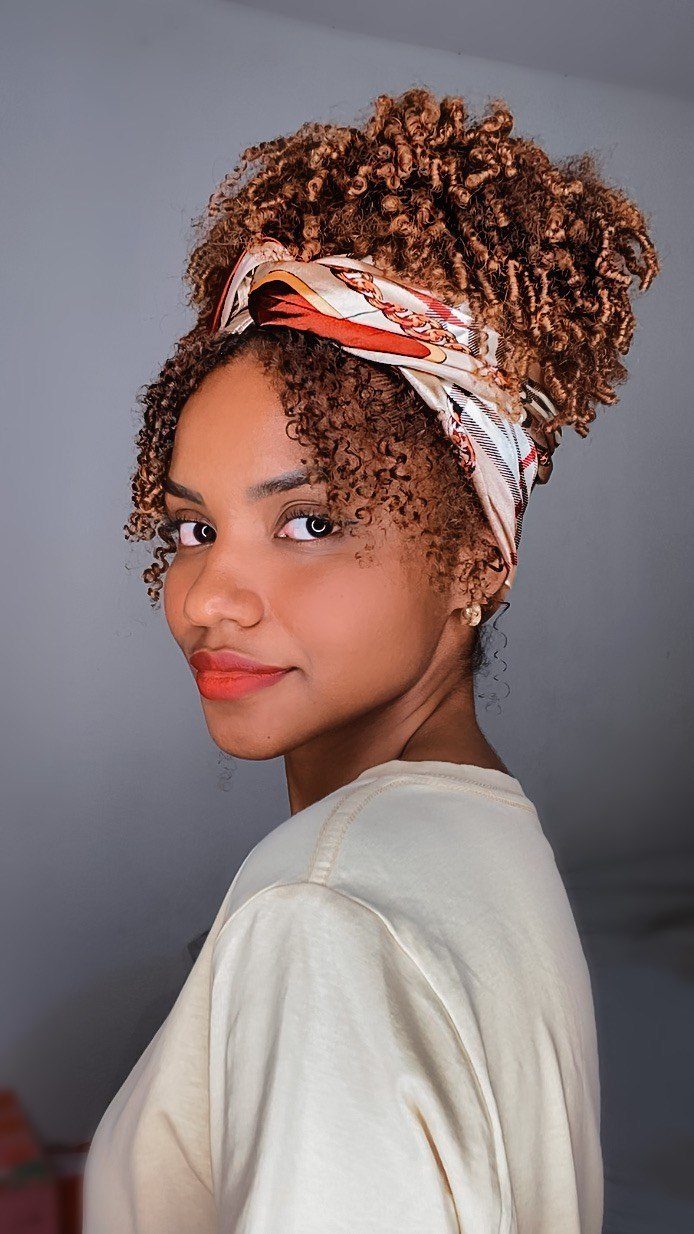 Woman wearing a patterned headwrap around a high curly puff with front curls left loose