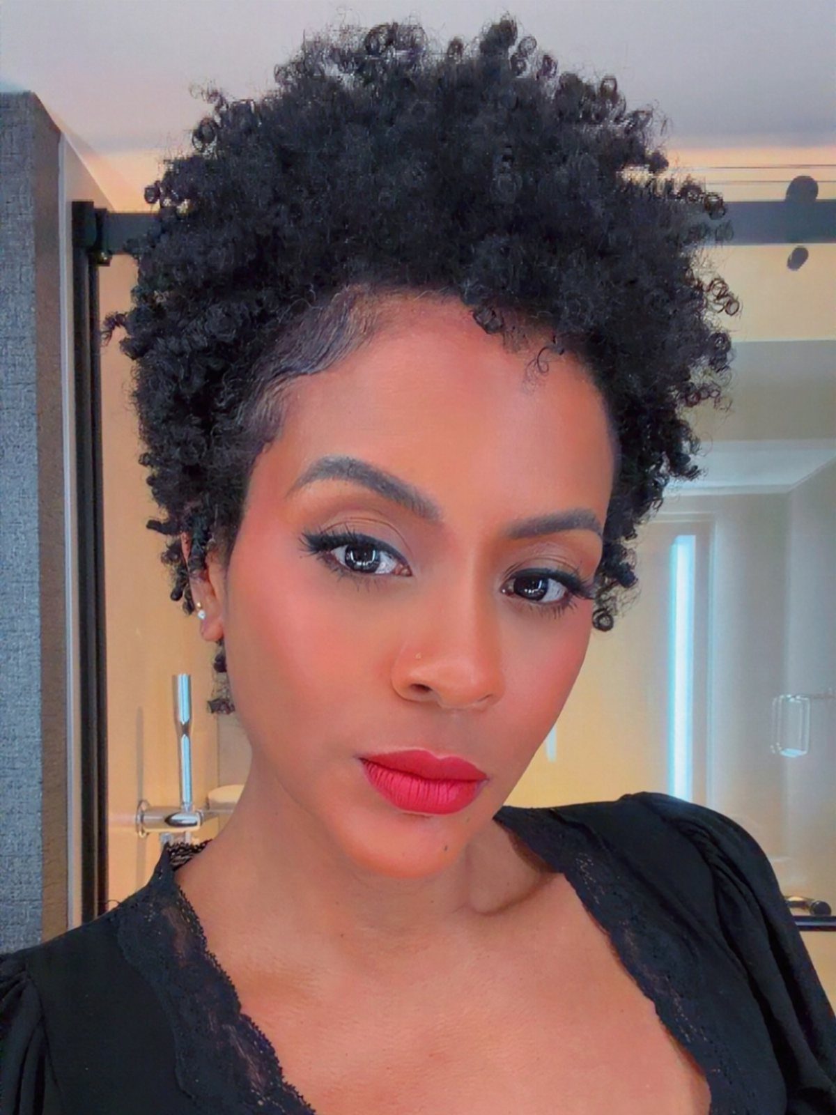 Woman wearing a short natural Afro with defined curls and red lipstick