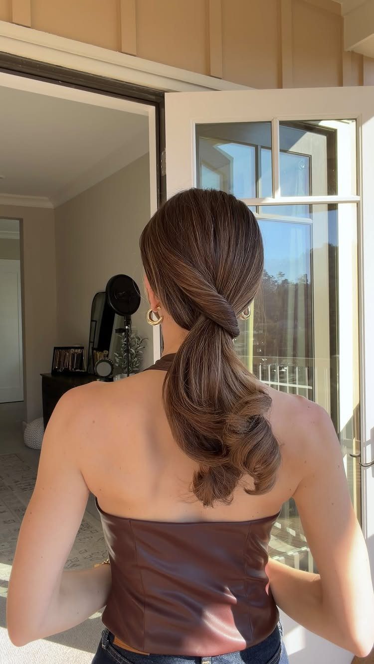 Low twisted ponytail with loose curls worn by a woman indoors
