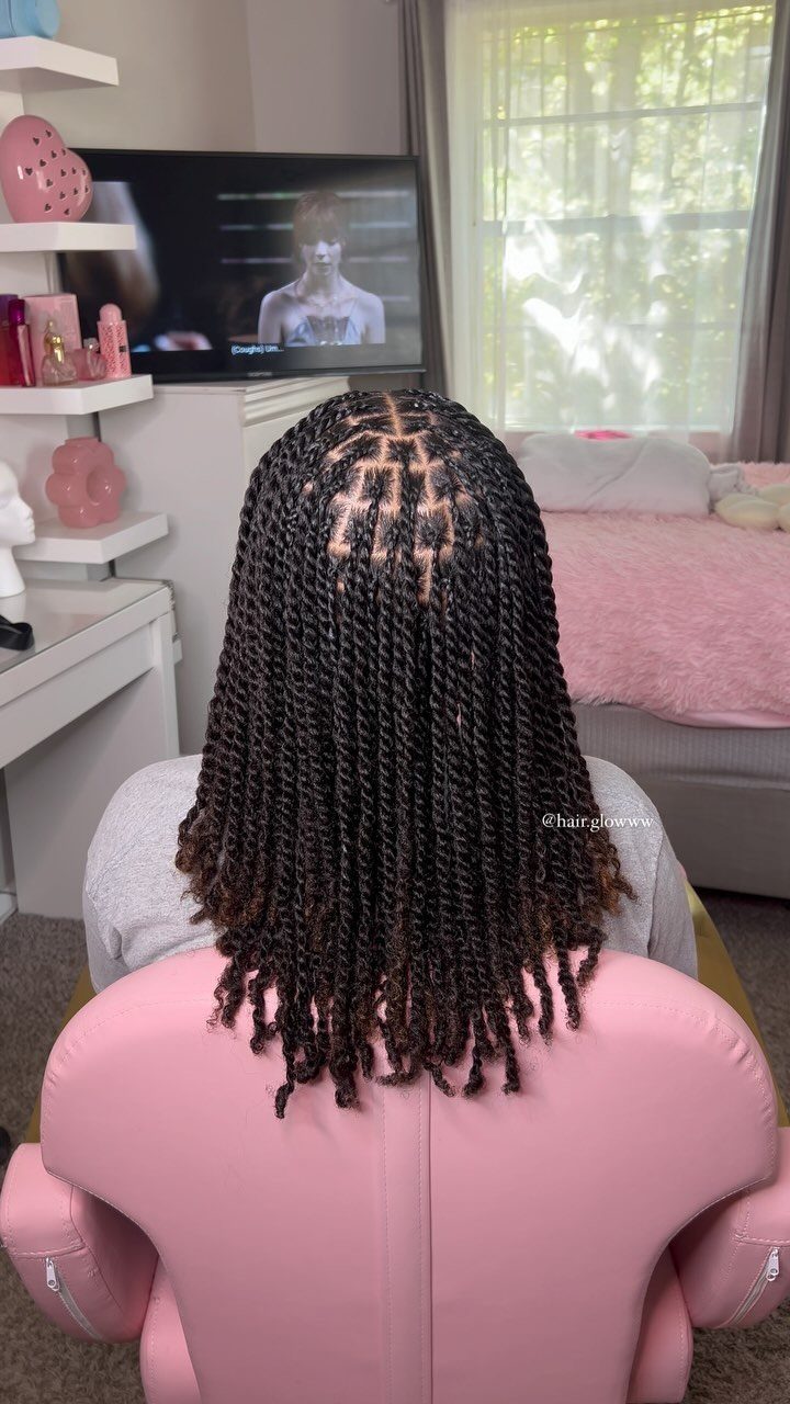 Long black twists fall from neat square parts on a seated person's head