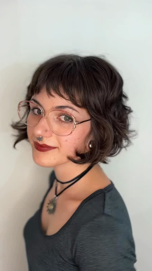 Person posing with a short dark curly bob and a wispy fringe