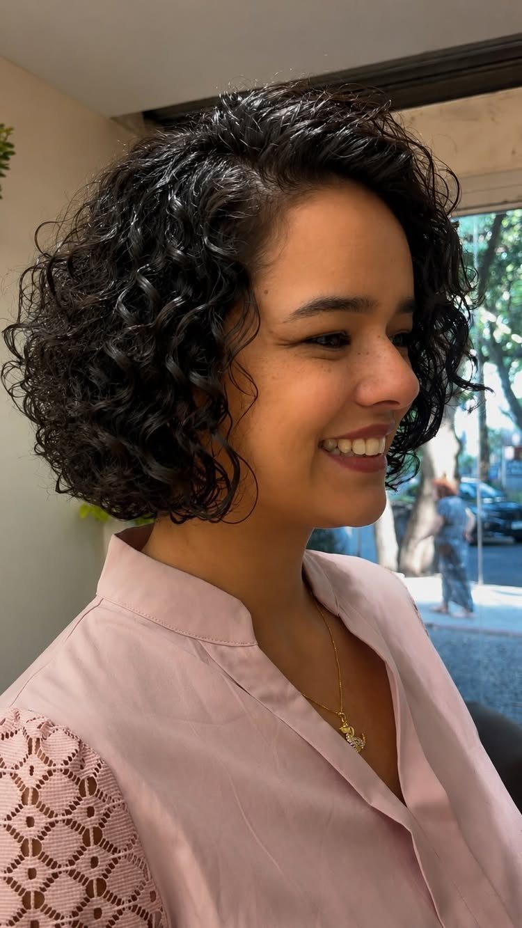 Woman with short dark curls wearing a rounded bob and pale pink blouse