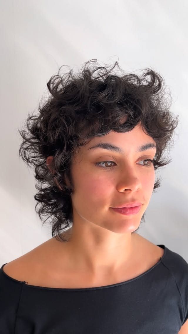 Curly mullet with tousled dark curls, short bangs, and longer hair at the back