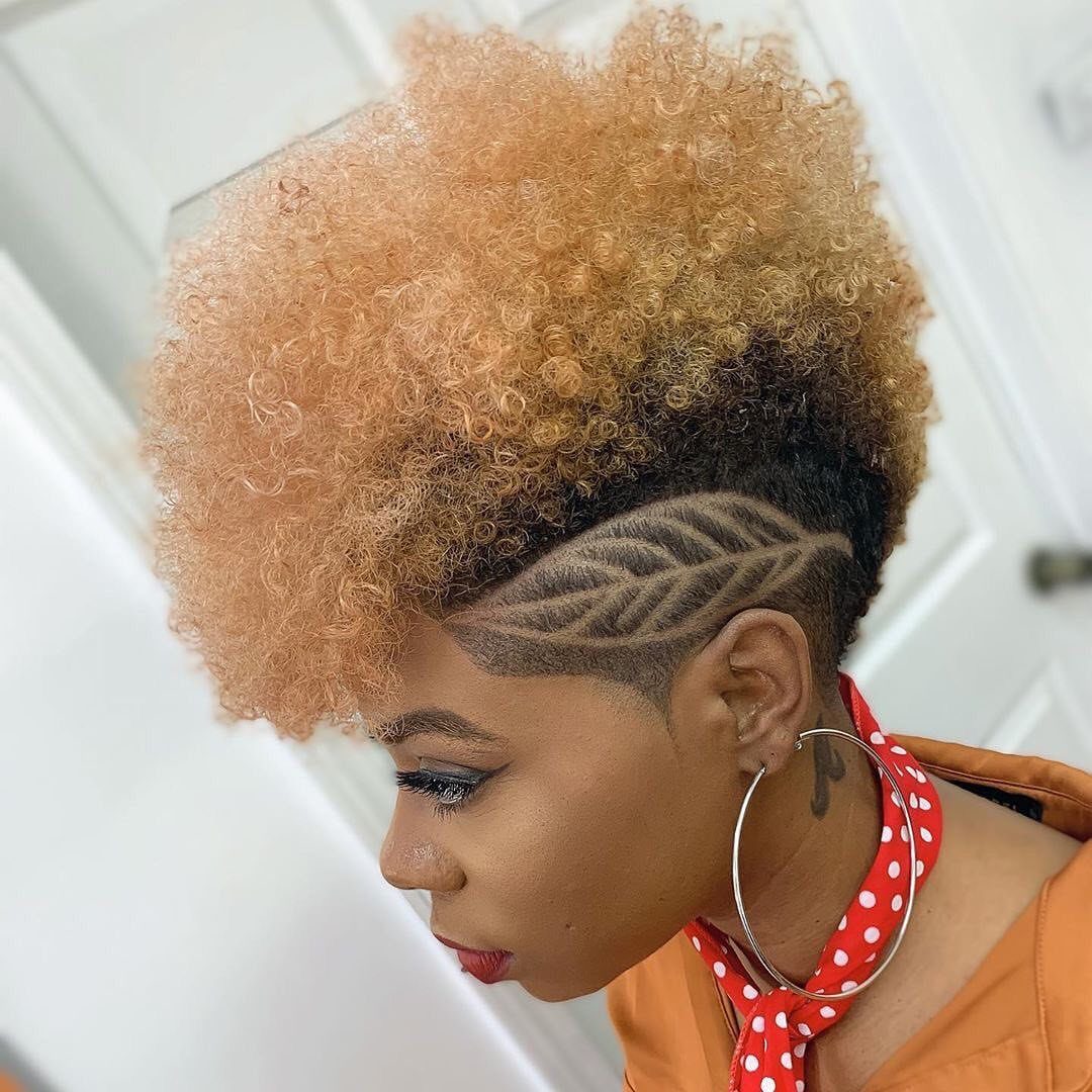 Tall peach curls rise above shaved, patterned sides in a faux hawk