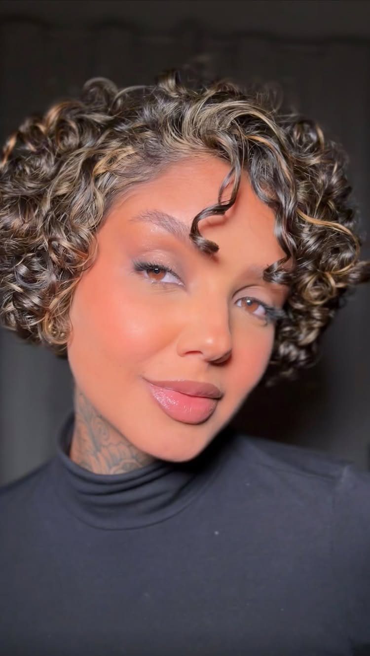 Woman with a short curly bob, dark roots, and blonde-tipped curls