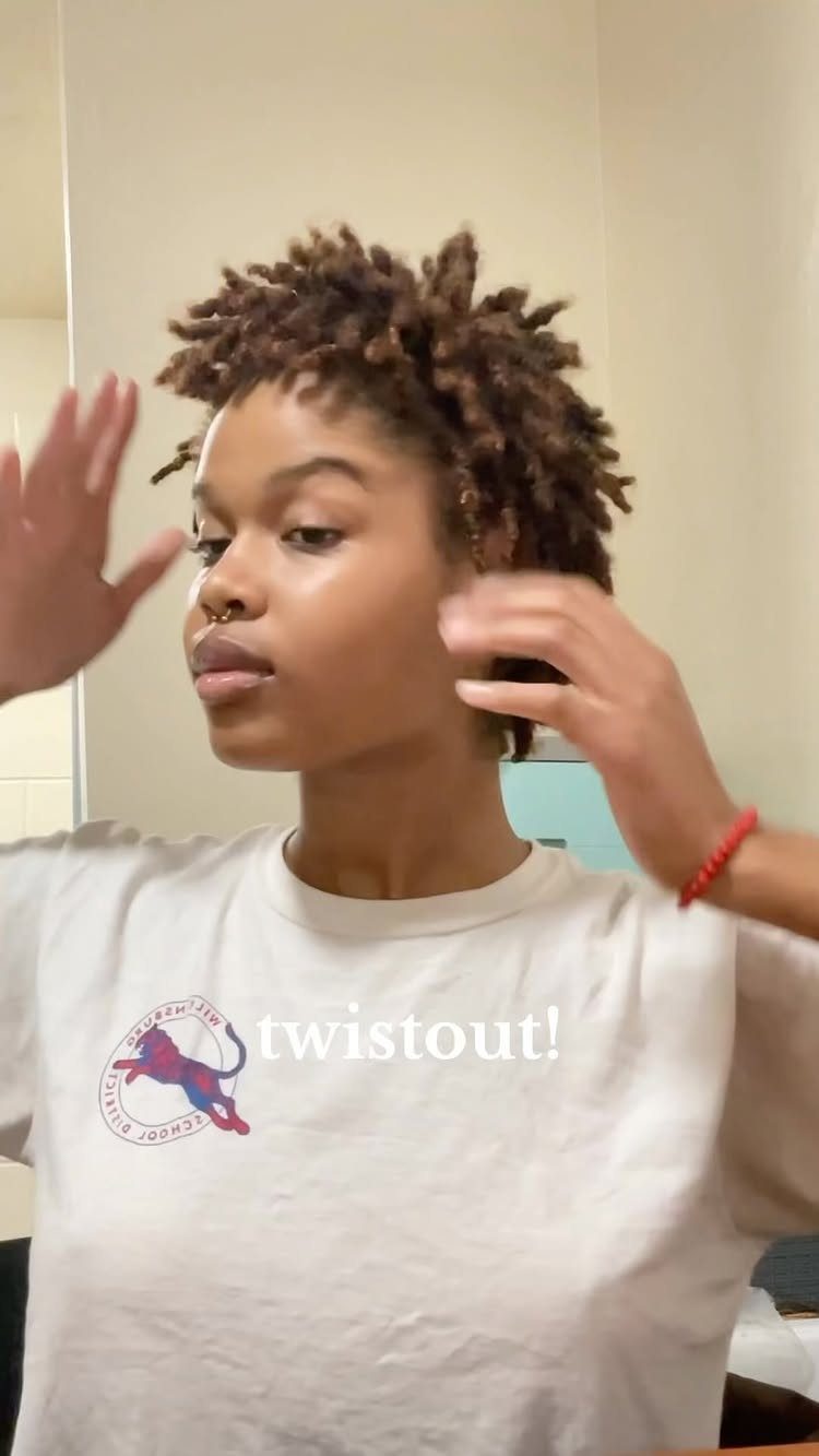 Person touching short, defined dark curls in a white shirt