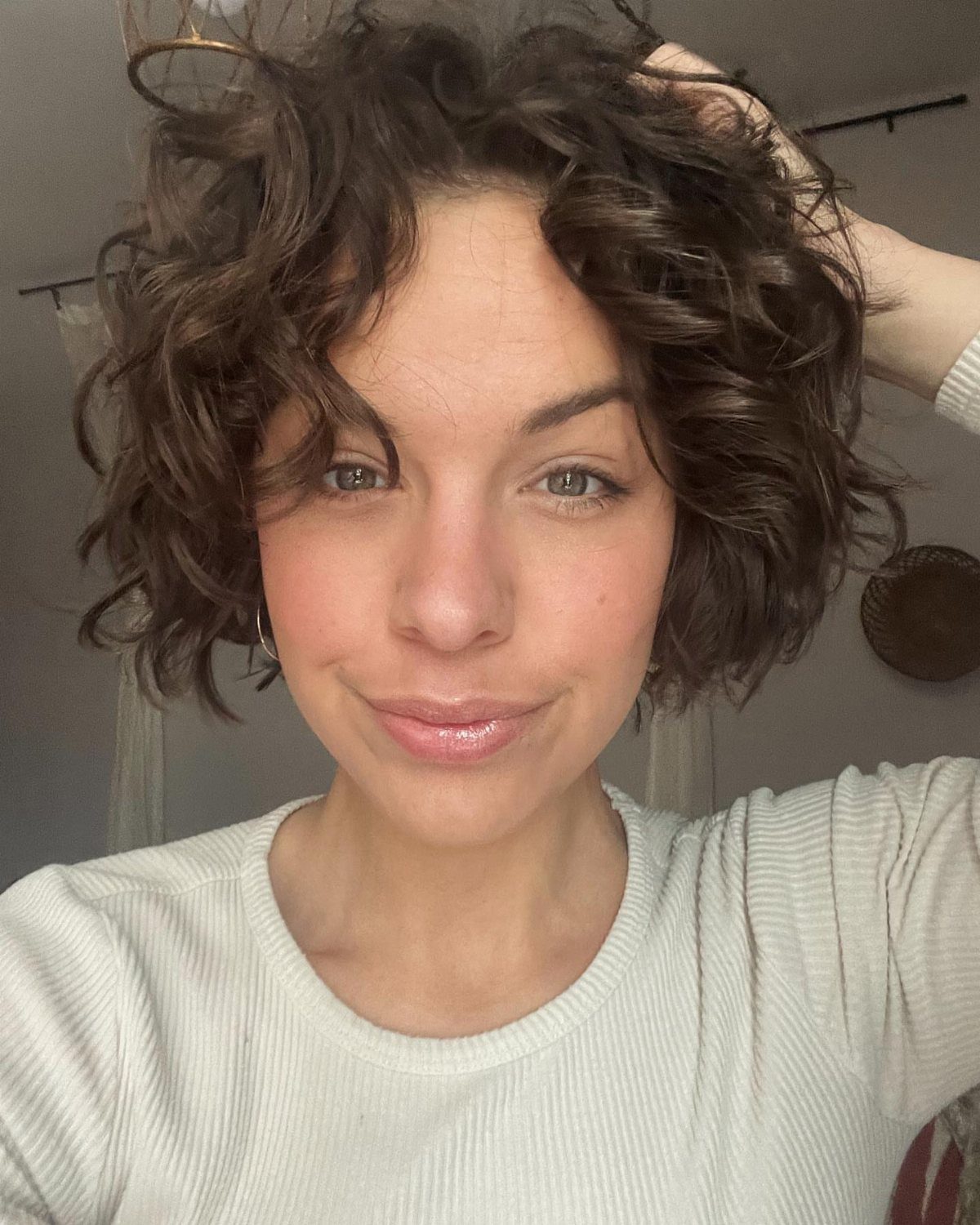 Woman showing short, natural dark curls in a casual indoor selfie