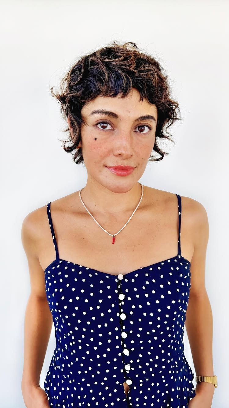 Woman with short dark curls and a curly fringe wearing a navy polka-dot dress
