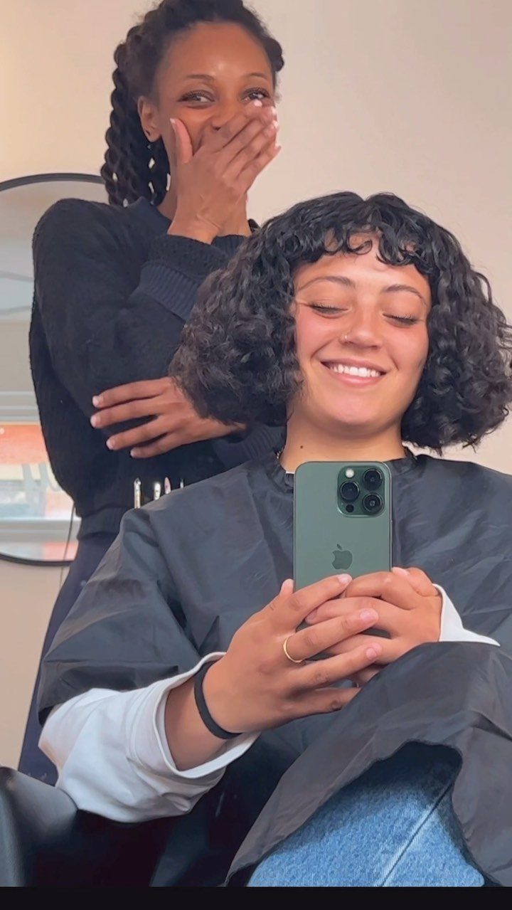 Short curly bob with micro bangs visible in a salon mirror selfie