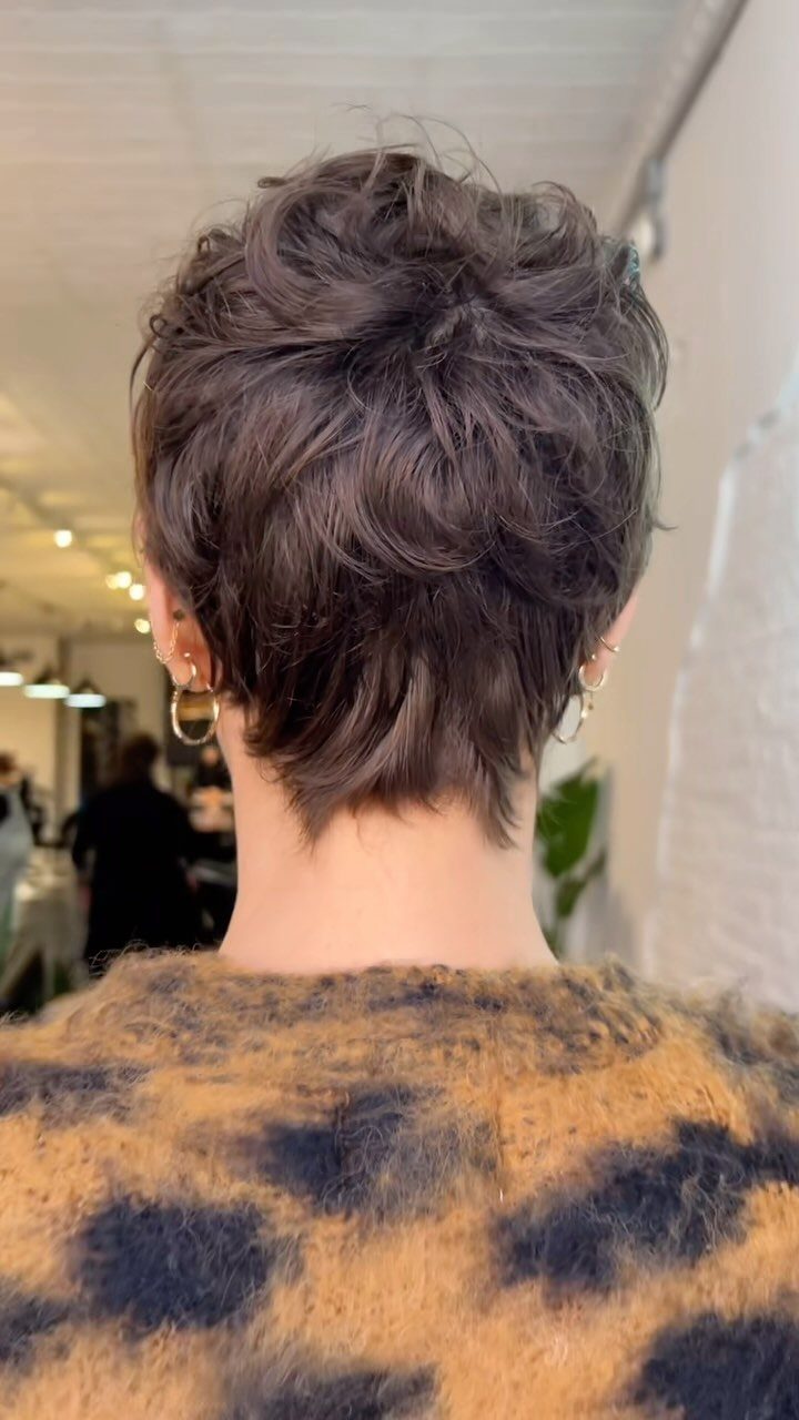 Short dark curls form a layered pixie cut above a patterned top