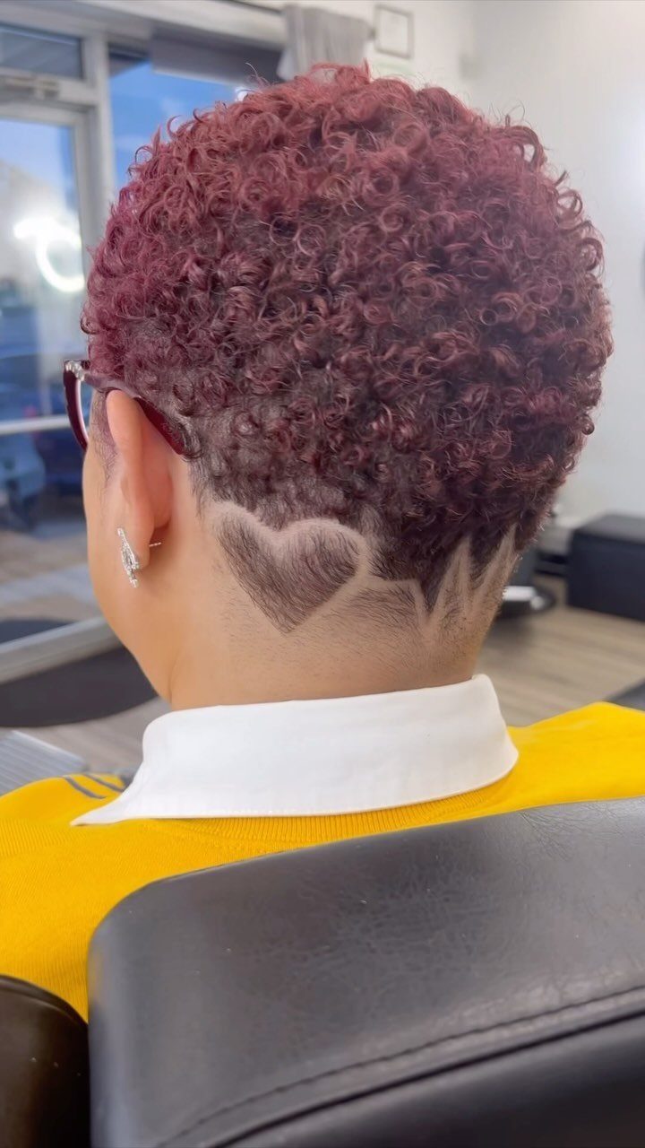 Burgundy curls contrast with shaved sides and a heart design at the nape