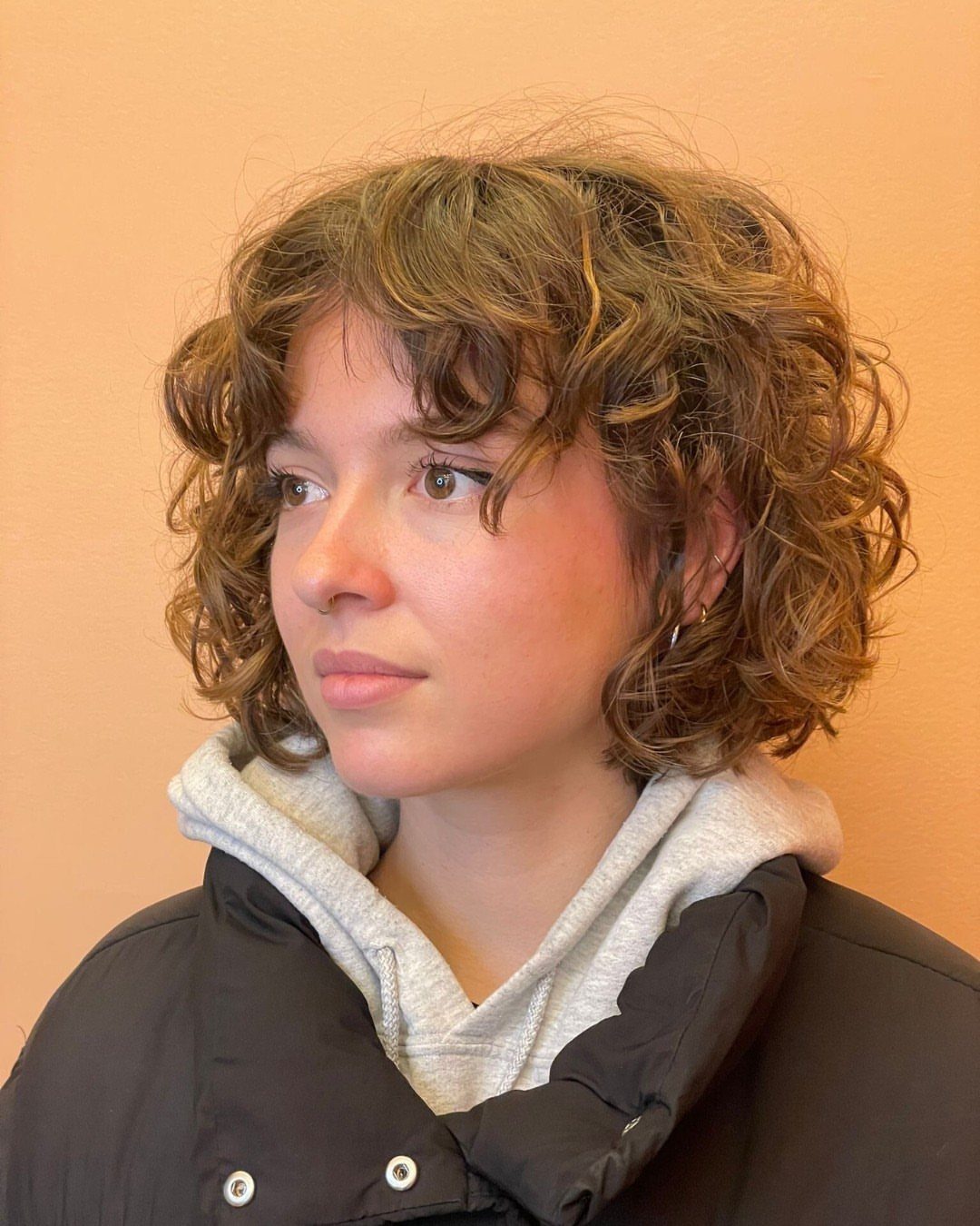 Short curly fringe frames a person’s forehead in a voluminous brown hairstyle