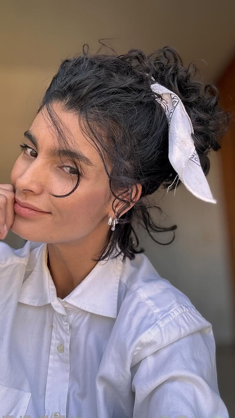 Woman with a loose curly updo, face-framing tendrils, and a white hair scarf