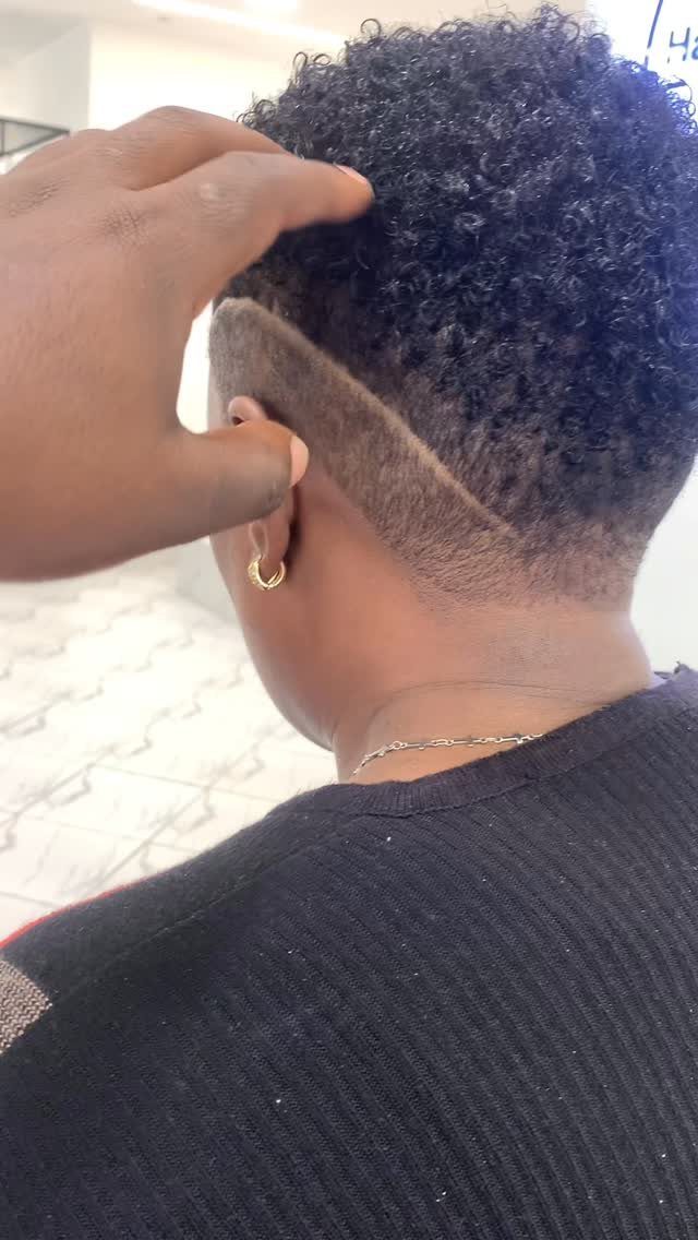 Short dark curls with slicked tapered sides and a shaved diagonal part