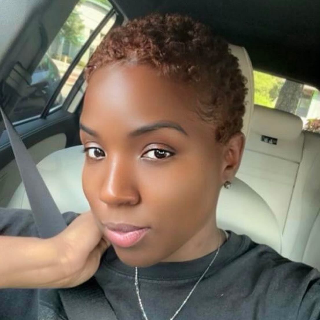 Person showing a short, tightly curled reddish-brown natural hairstyle in a car
