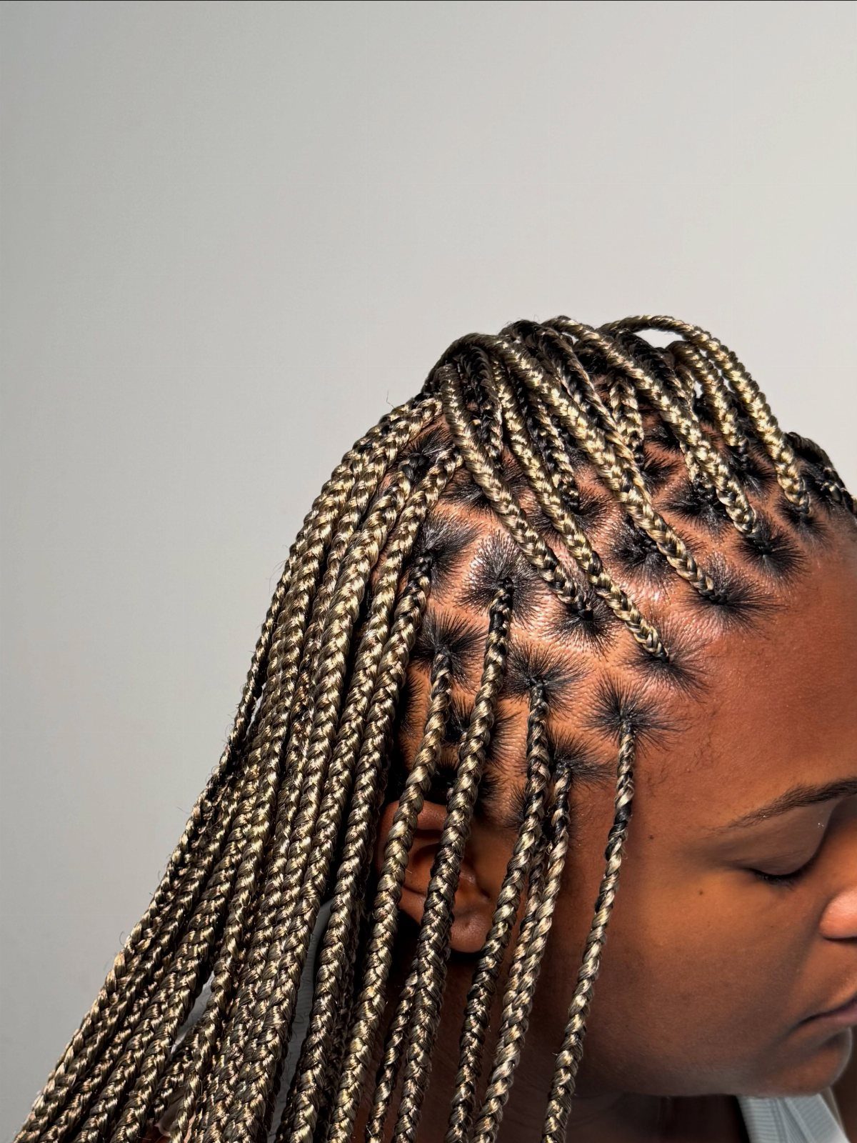 Fine ash-blonde box braids with neat scalp parts fall over one shoulder