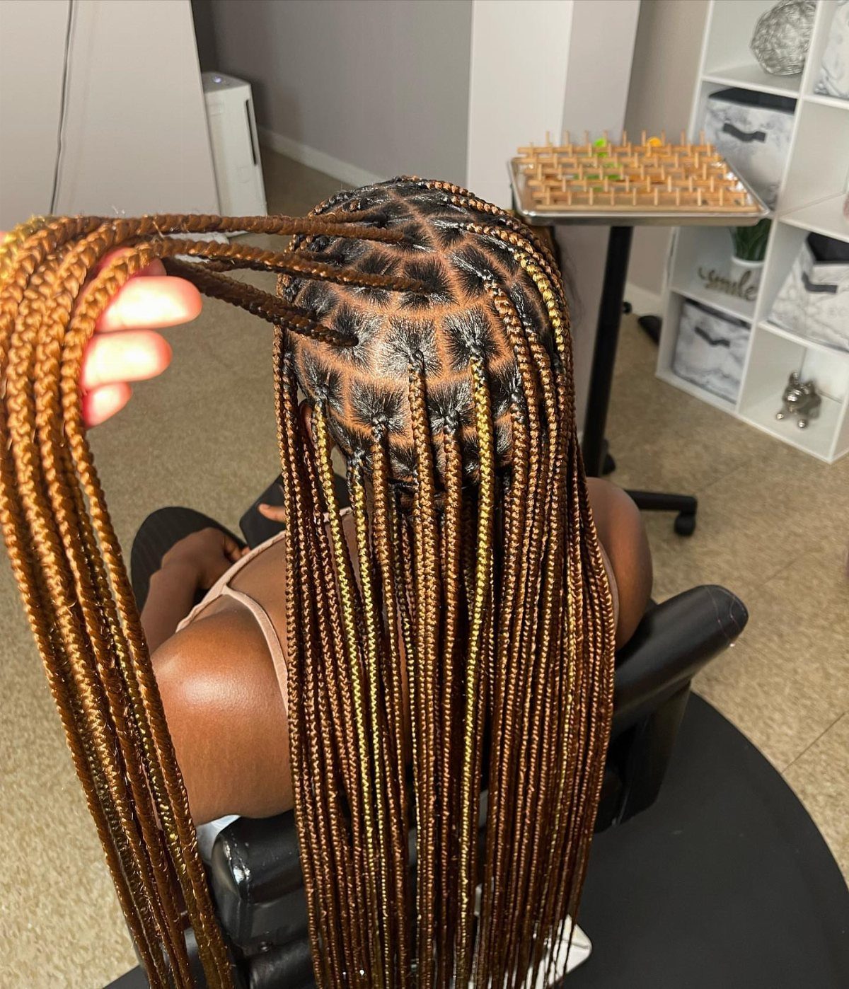 Narrow black and golden-brown box braids shown from the back in a salon
