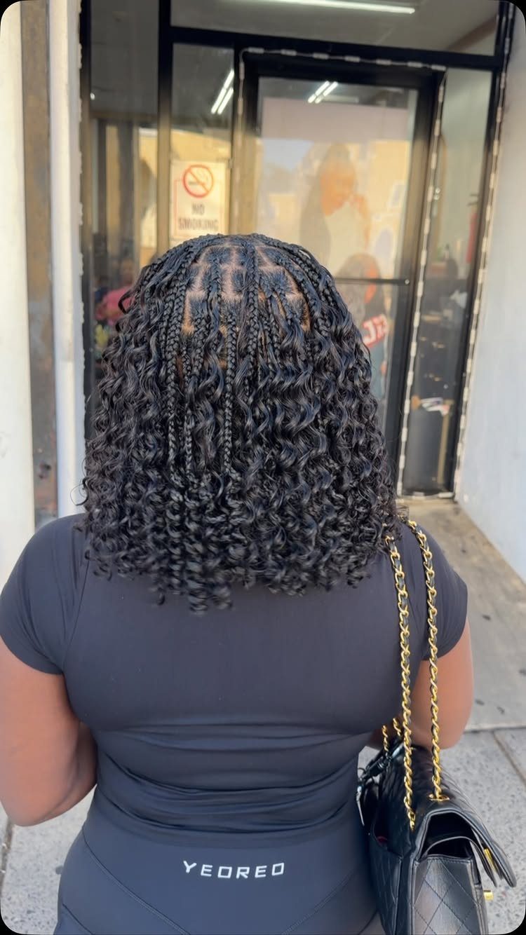 Short curly-ended black box braids styled into a bob outside a storefront