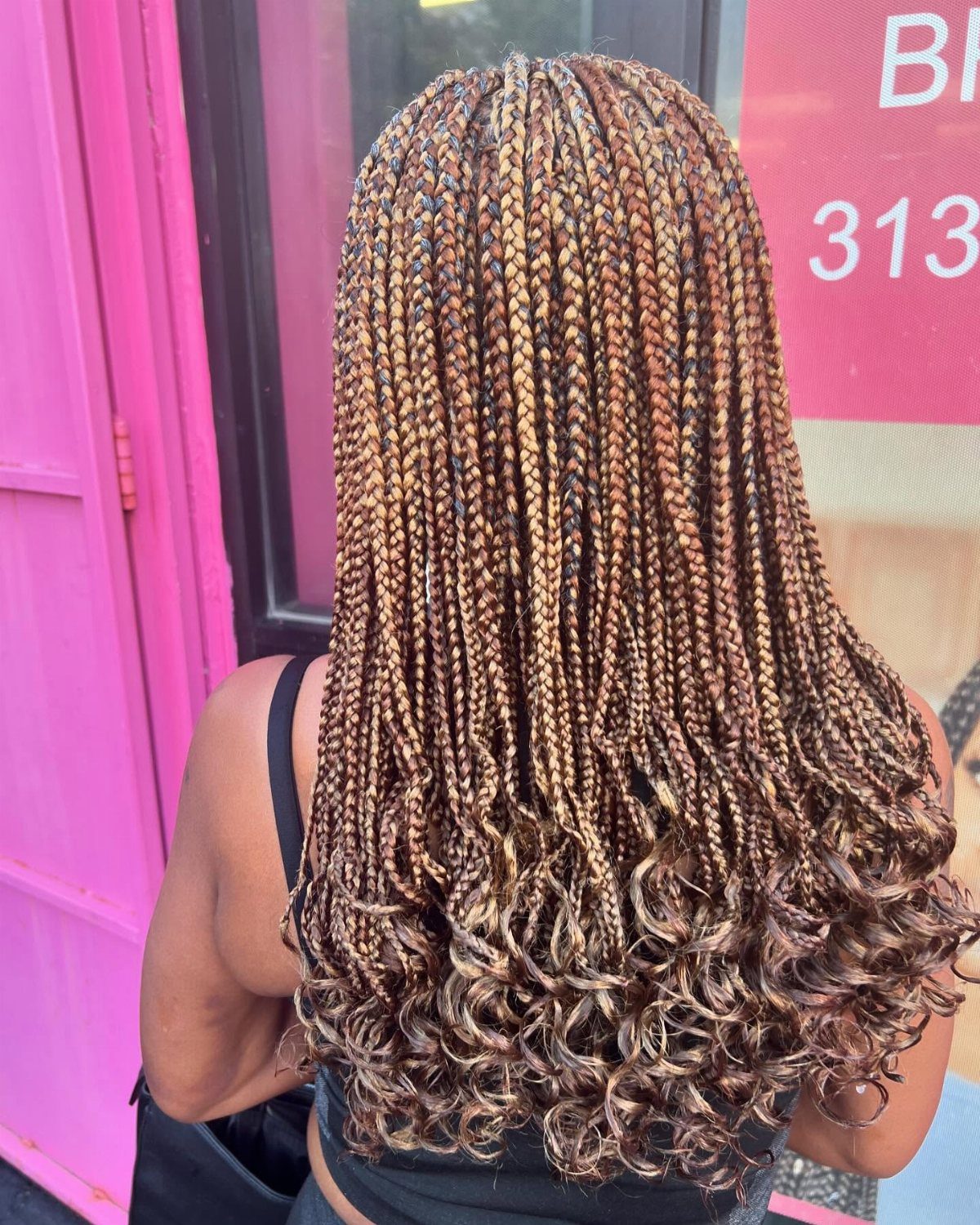 Long small blonde-highlighted box braids curl at the ends down a person's back