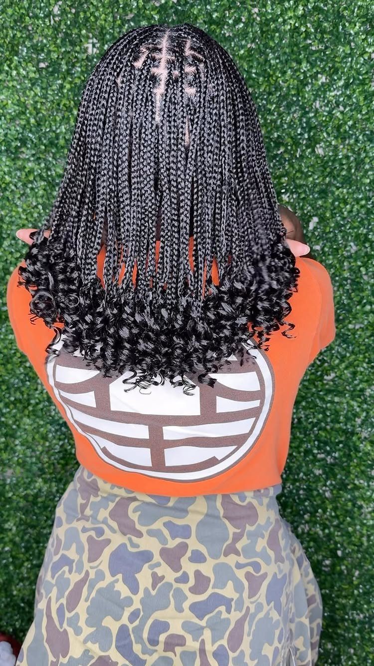 Black box braids with loose curly ends fall over an orange top