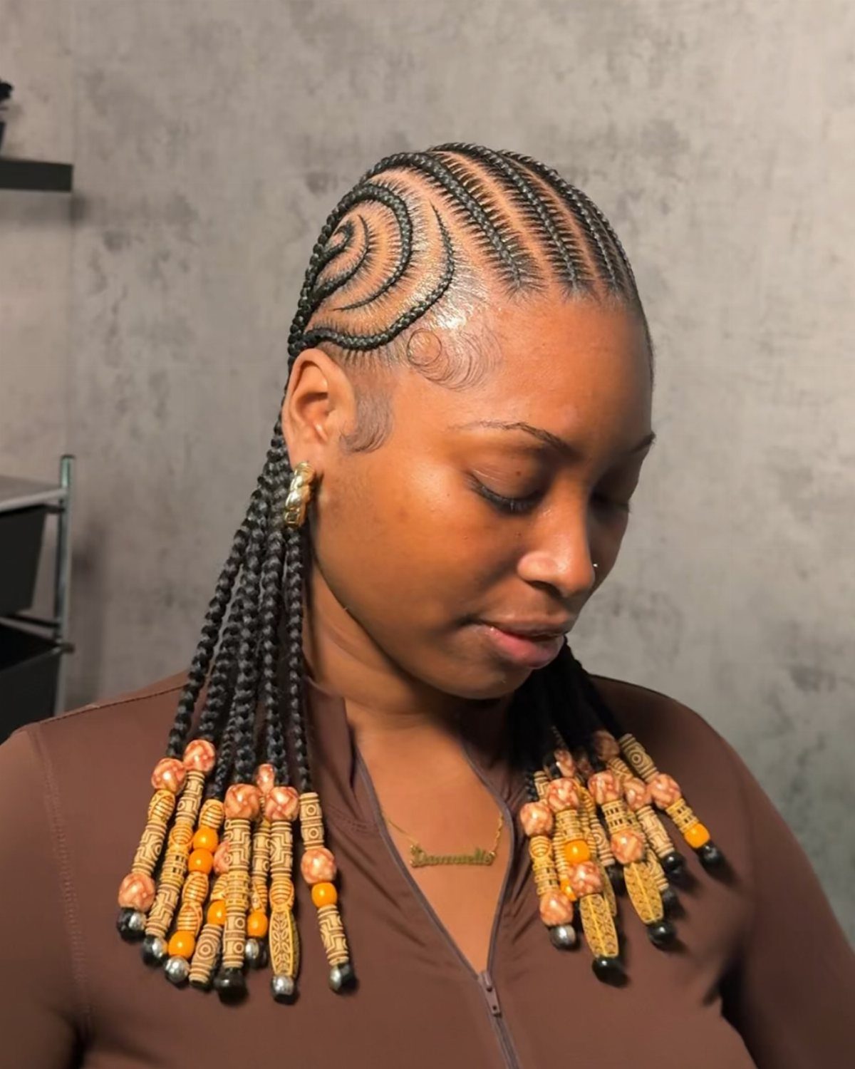 Feed-in cornrows curve across a woman's scalp into beaded braids