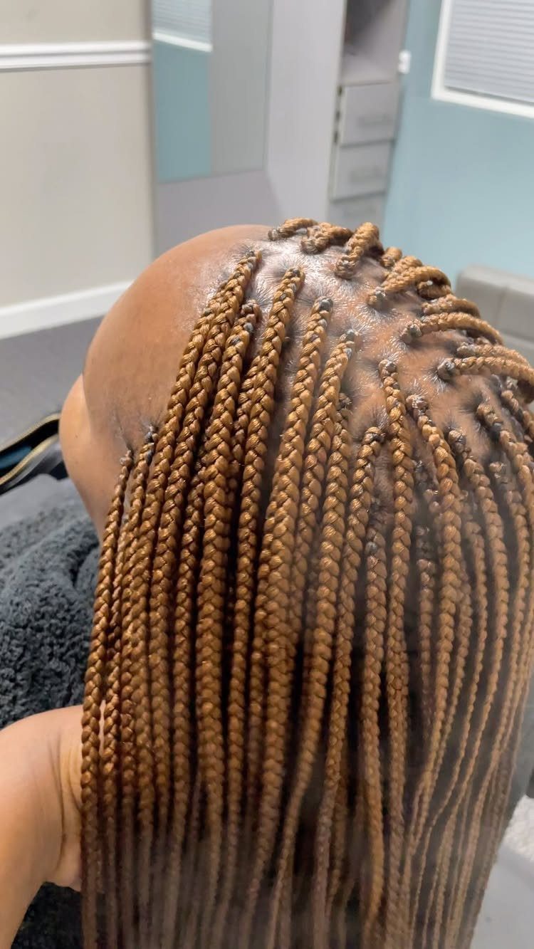 Small golden-brown box braids cover a person’s head in a salon