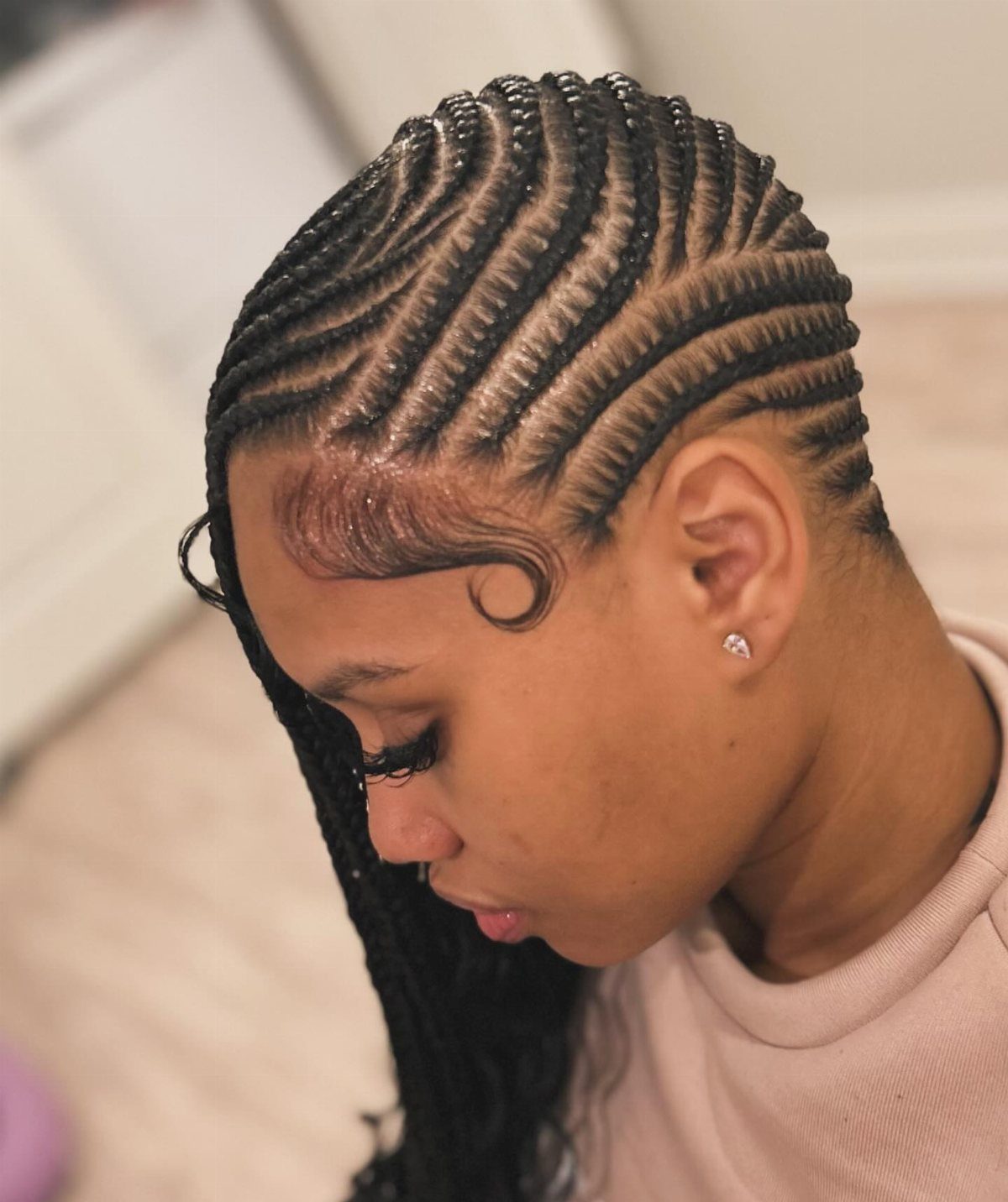 Side-swept black cornrows transition into long braids falling over one shoulder