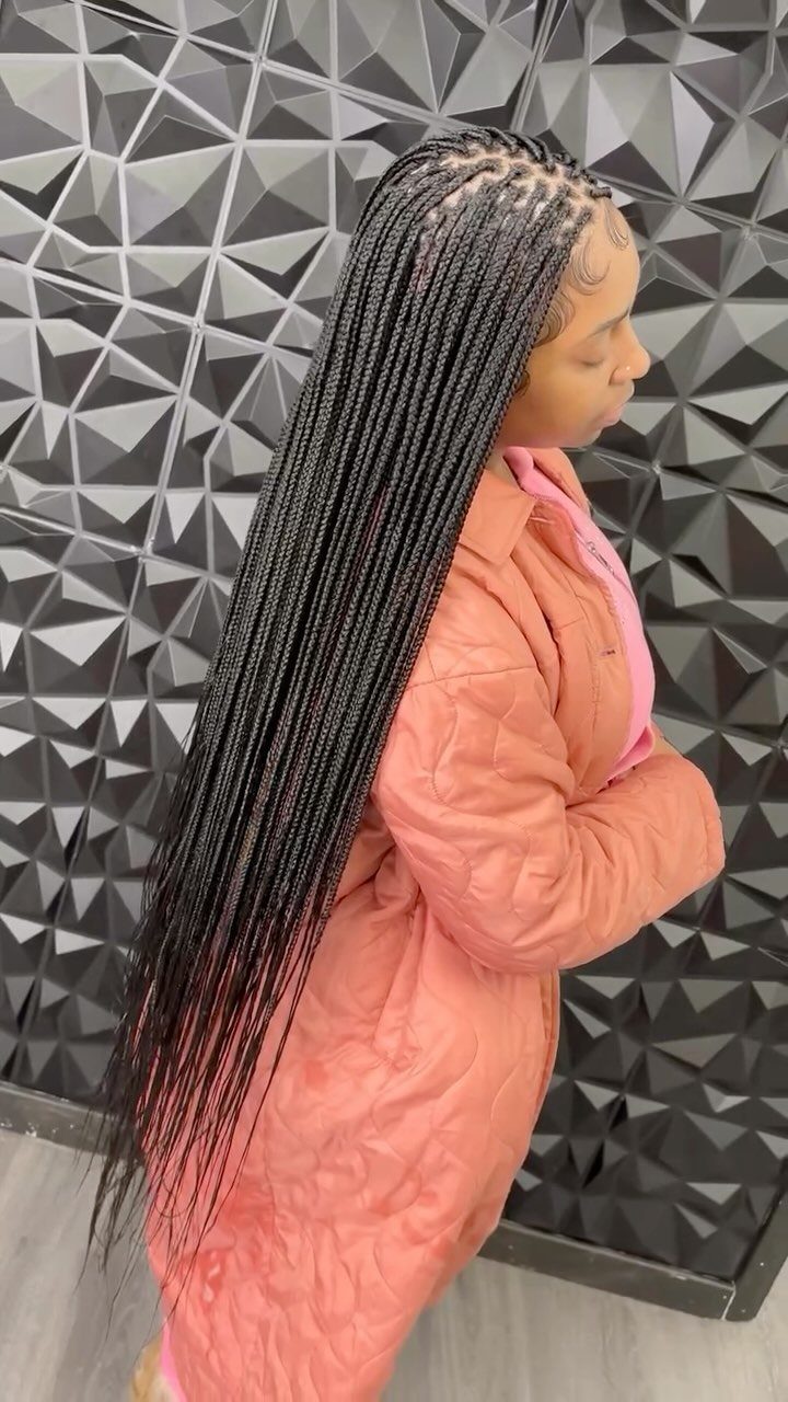 Woman wearing long, thin black box braids loose over a coral coat