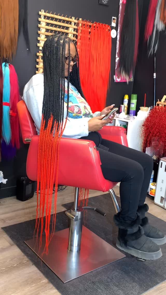 Woman seated in a salon wearing long black-to-red ombre box braids