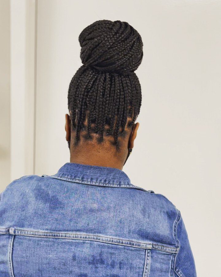 Black braids gathered into a high bun above a blue denim jacket
