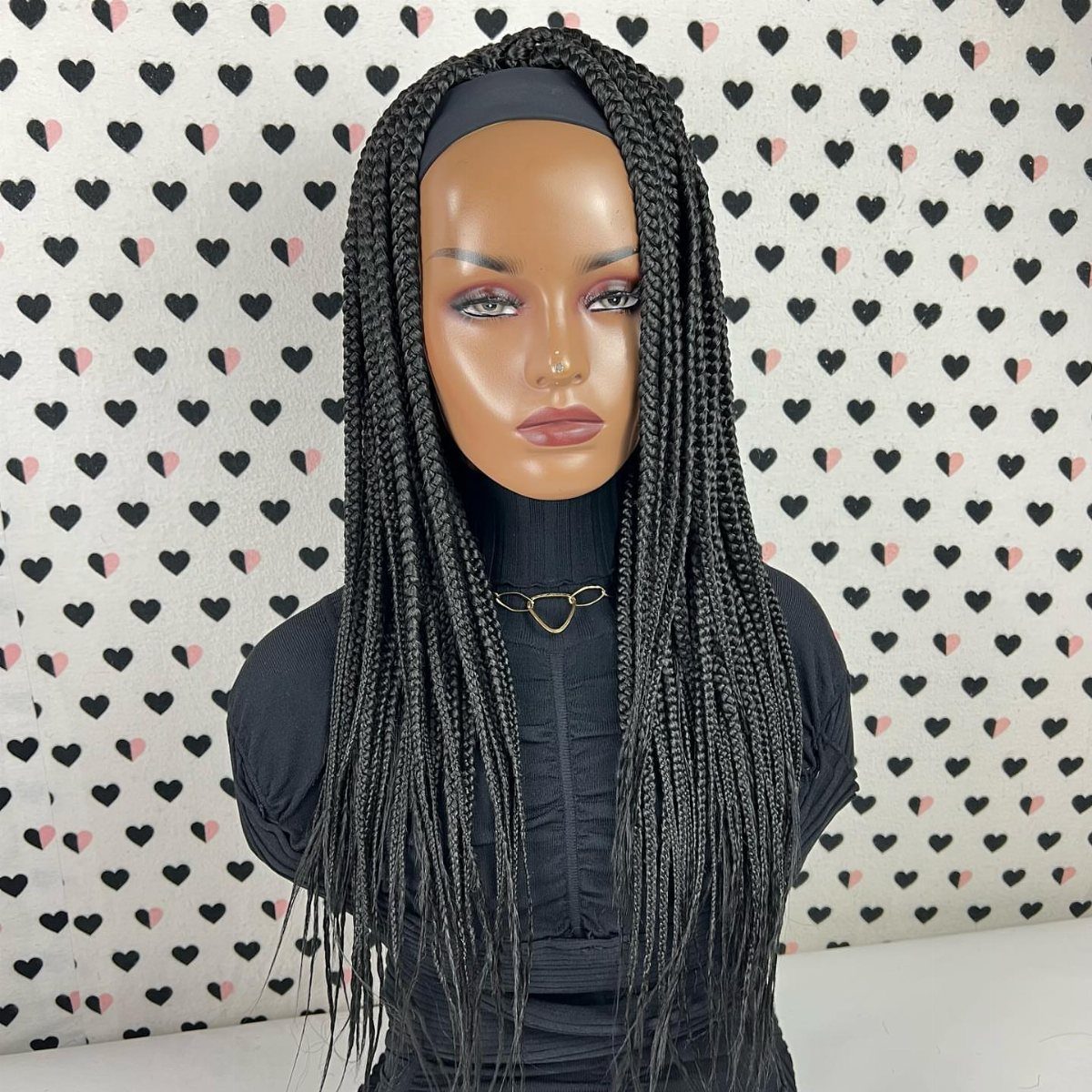 Mannequin wearing long, thin black box braids against a heart-patterned backdrop