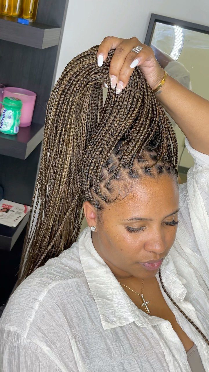 Small brown box braids gathered into a high ponytail and held by hand