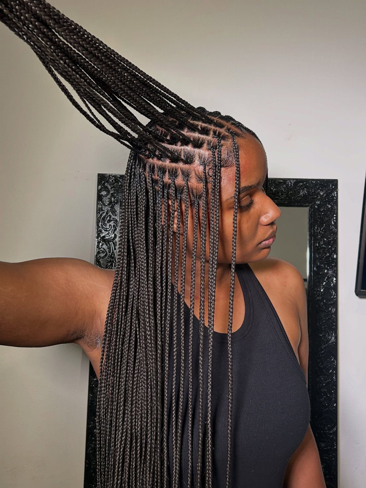 Woman displaying long, small black knotless braids with neat square parting