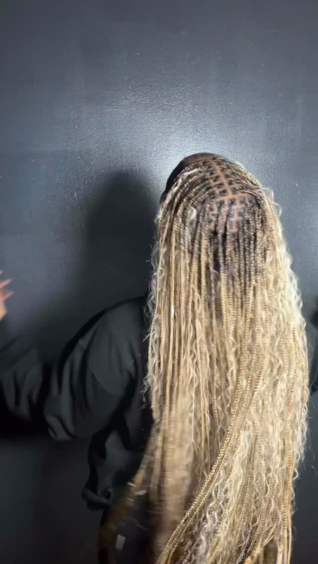 Long thin blonde braids with dark roots fall down a person's back