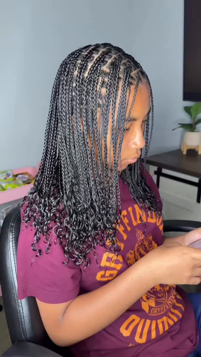 Small black knotless braids with curled ends worn over a purple T-shirt