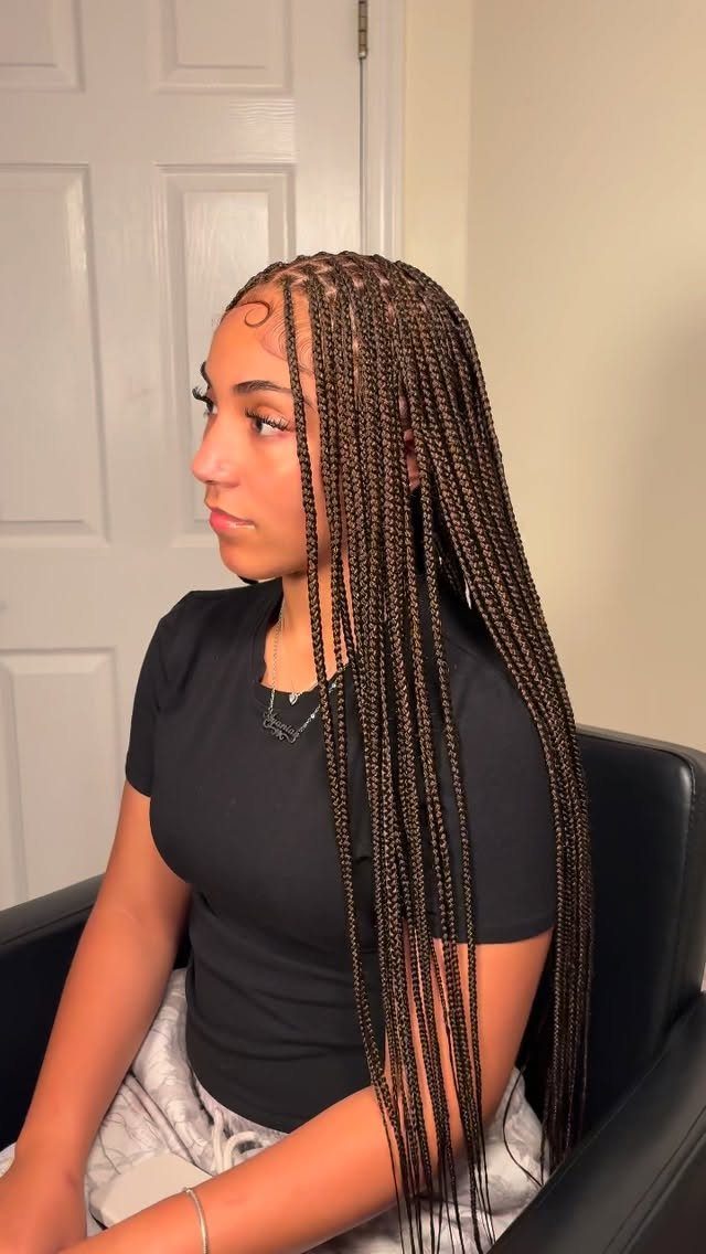 Woman wearing long, small dark brown braids while seated in a chair