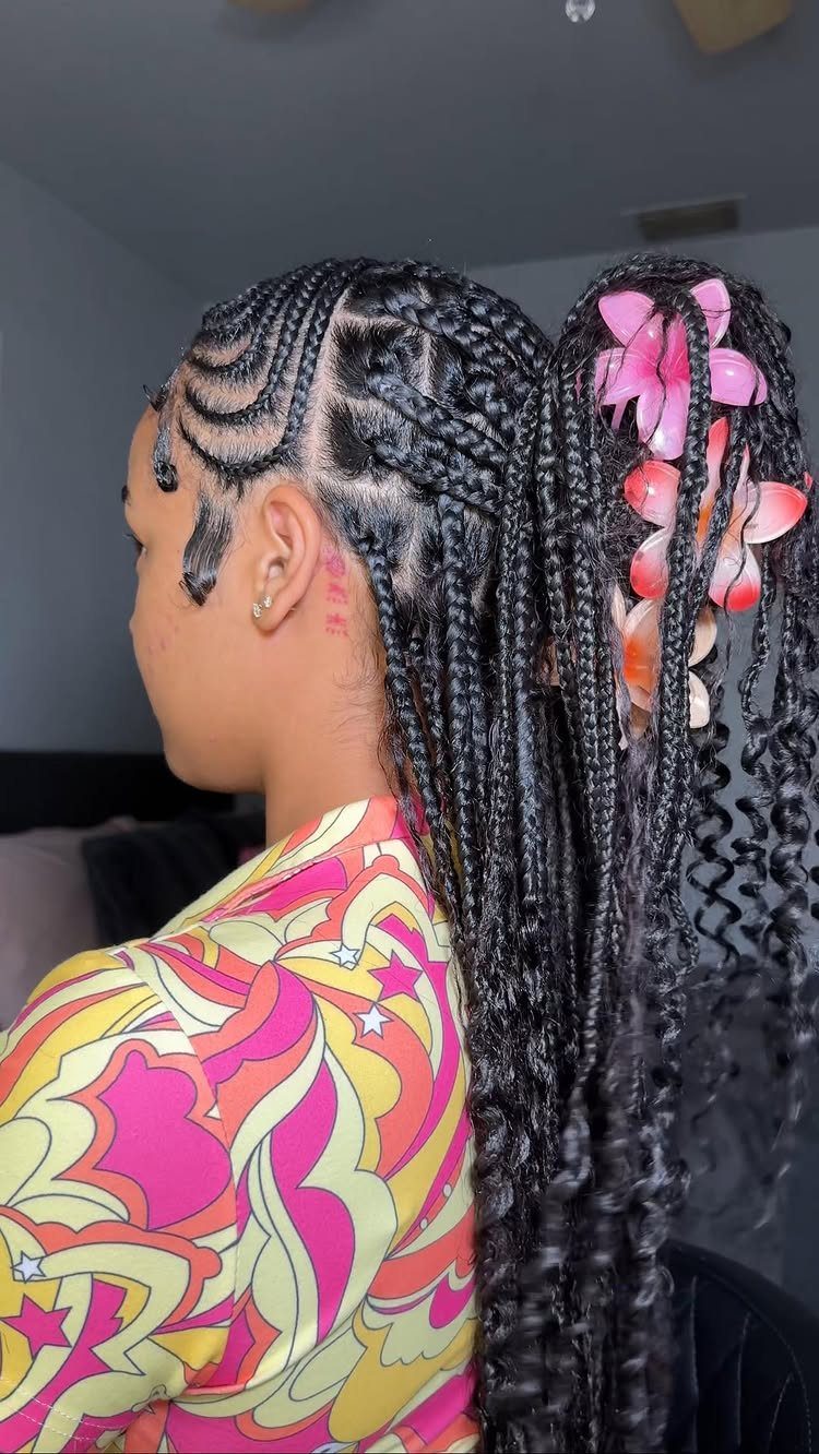 Long black braids with pink and red flower clips cascade over a colorful patterned top