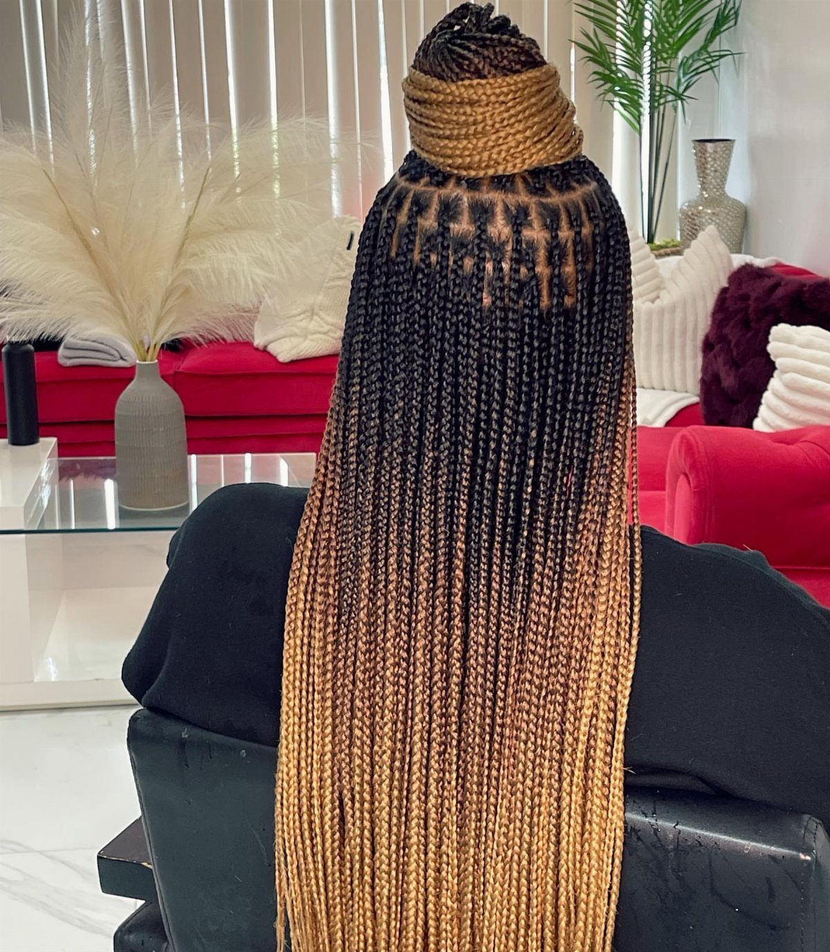 Long small braids transition from dark roots to golden blonde ends, gathered in a high bun