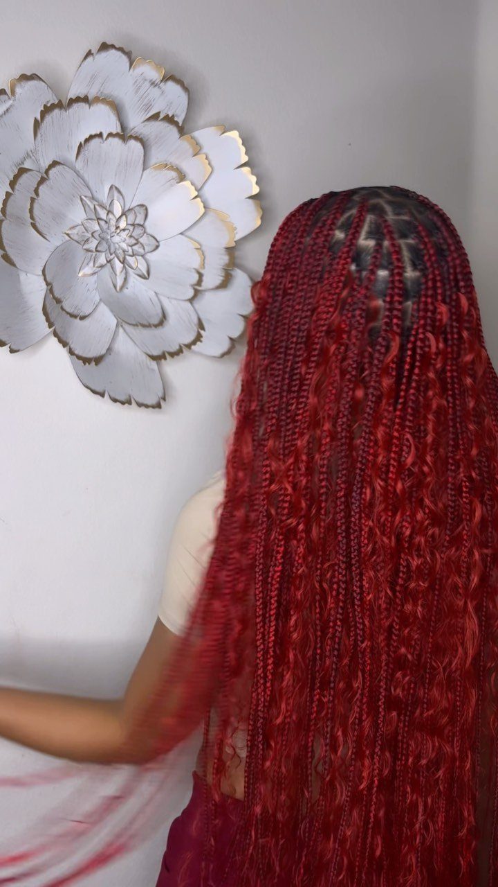 Long burgundy-red braids cascade down a person's back beside a white flower wall ornament