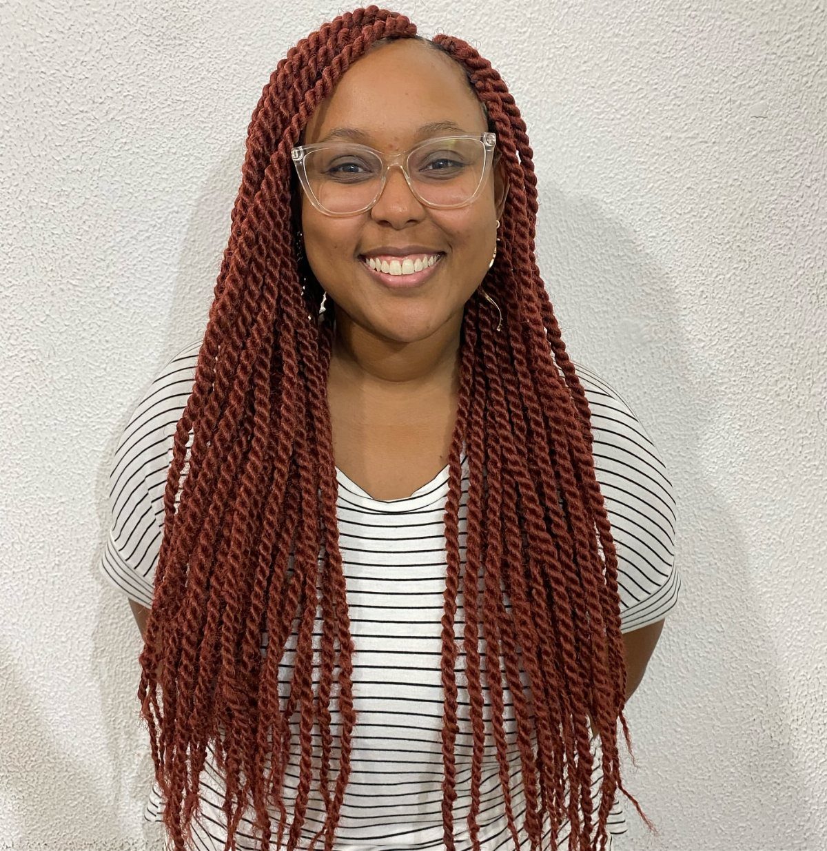 Woman wearing long deep red Marley twists against a light textured wall