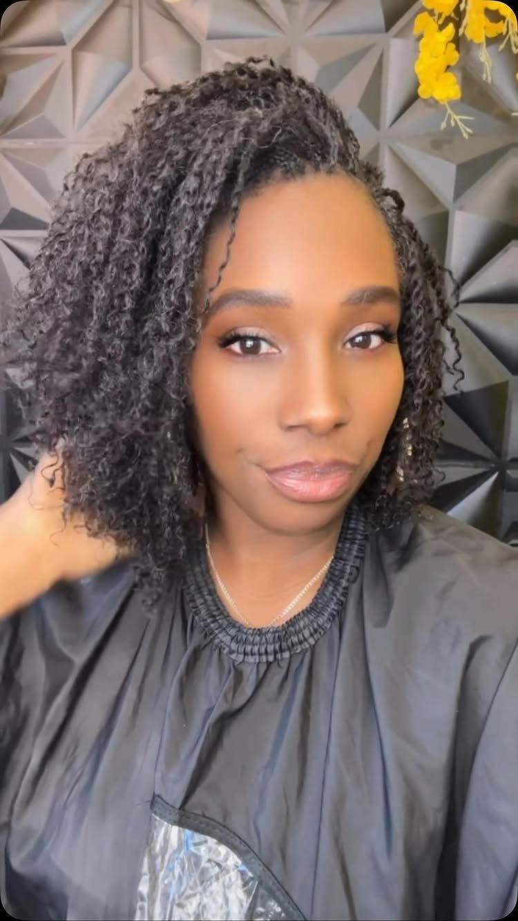 Woman poses with shoulder-length dark finger twists in a black salon cape