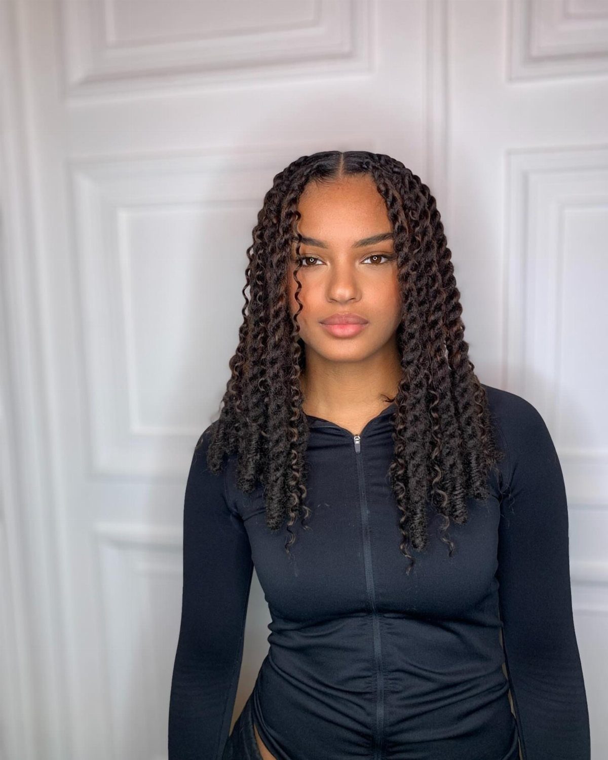 Woman wearing long dark Marley twists against a white paneled wall
